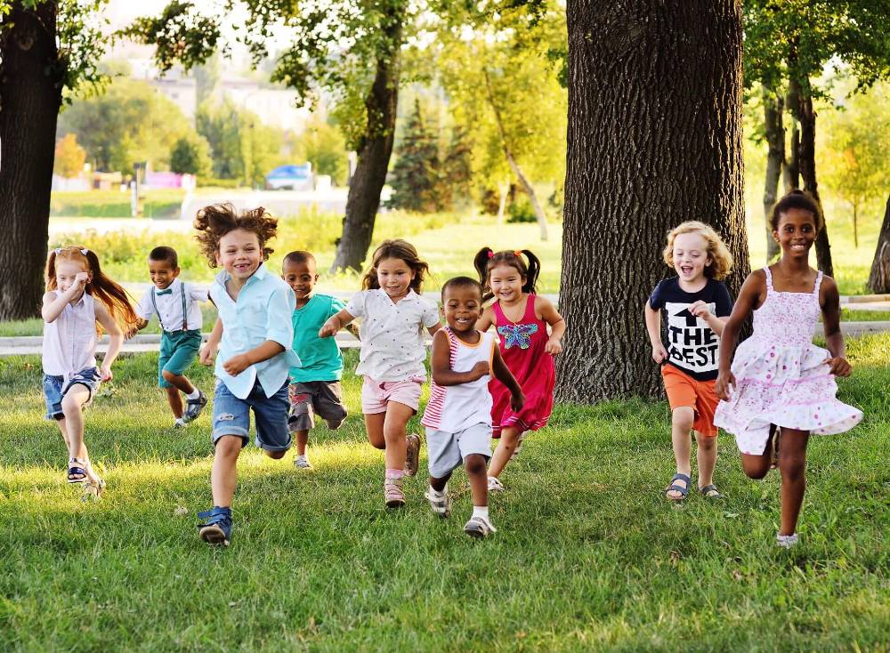 A group of happy diverse children of boys and girls run in the Park on the grass on a Sunny day at summer camp