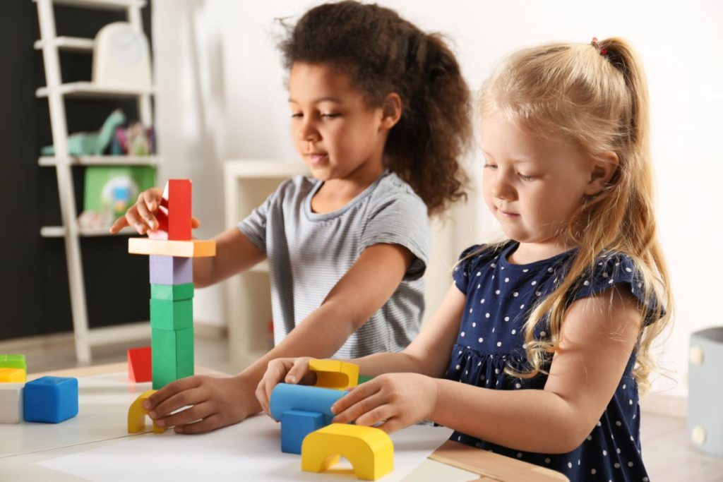 Two toddler girls playing with building blocks in kindergarten